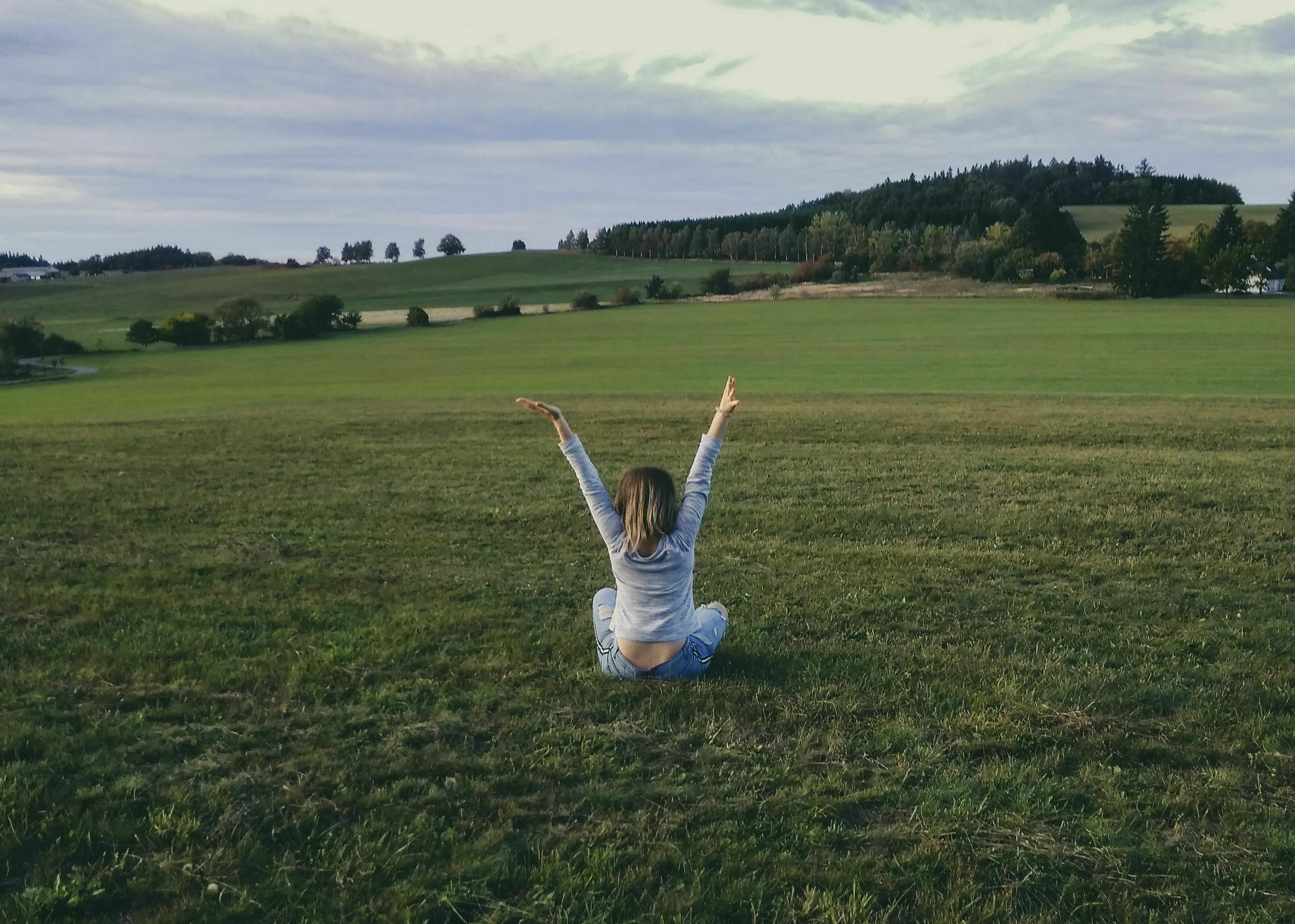 A woman sits with arms raised in a field, symbolizing a life well lived as a historical figure.