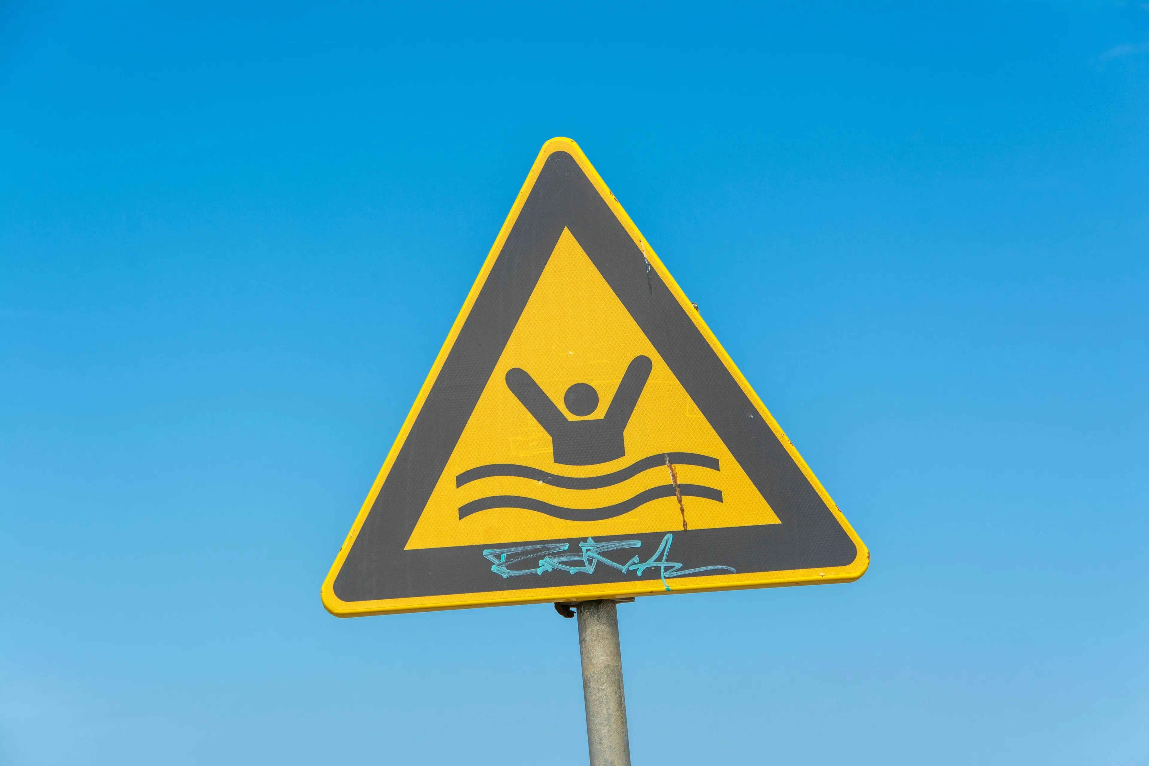 A yellow triangular sign with a drowning person icon against a blue sky for the Historical Figure quiz: How do you respond to a genuine crisis?