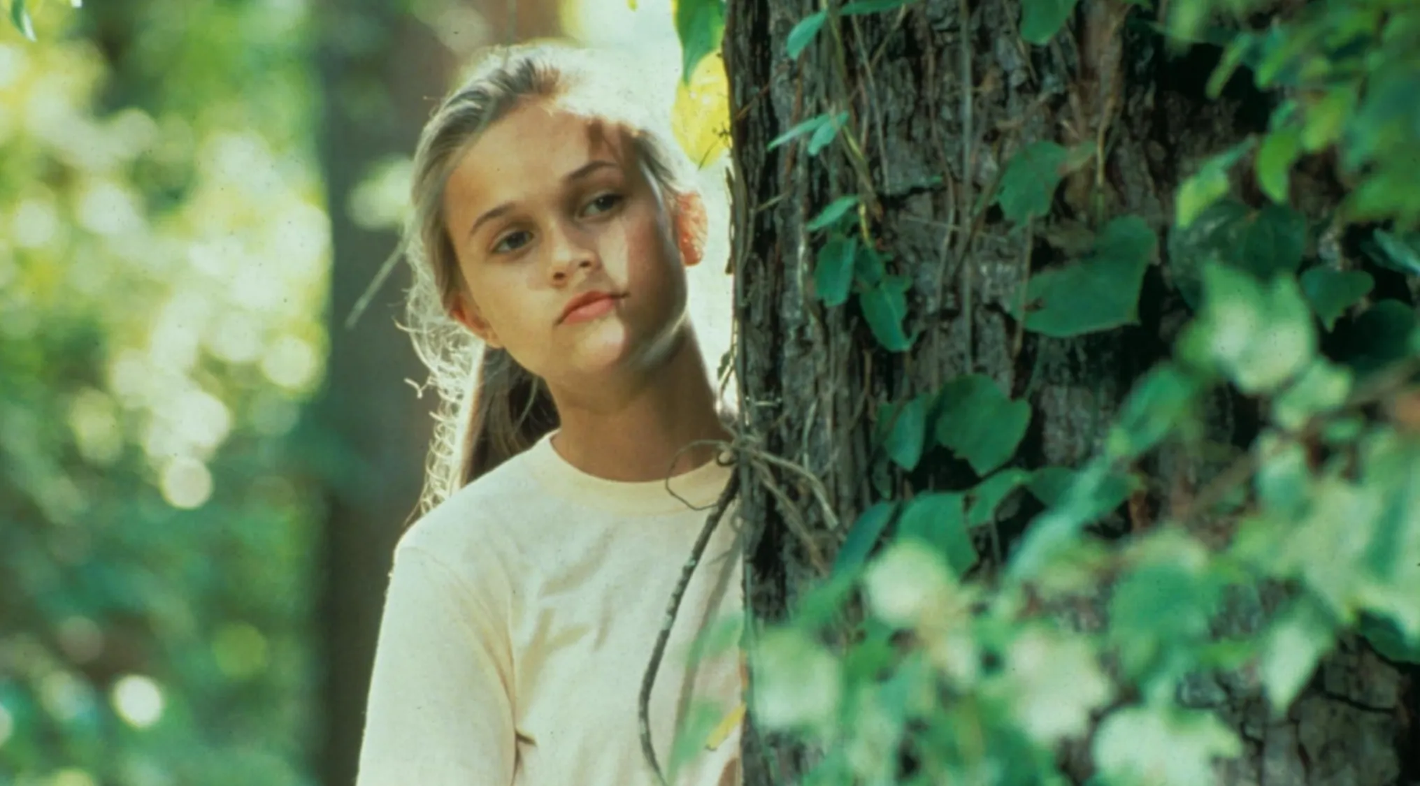 Young Reese Witherspoon in her film debut, looking contemplative by a tree.