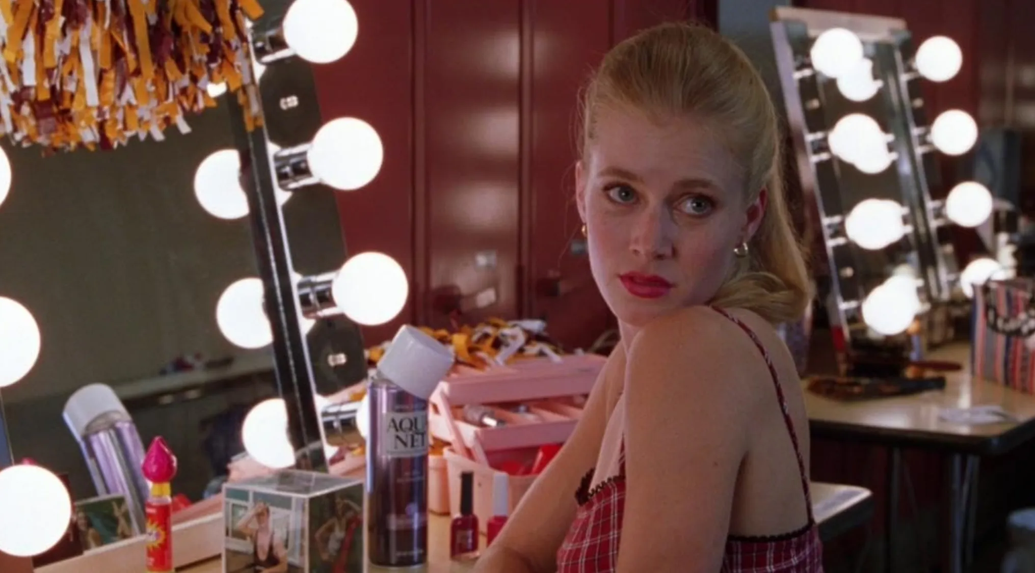 Amy Adams in her film debut for Drop Dead Gorgeous sitting at a brightly lit makeup vanity, looking over her shoulder.