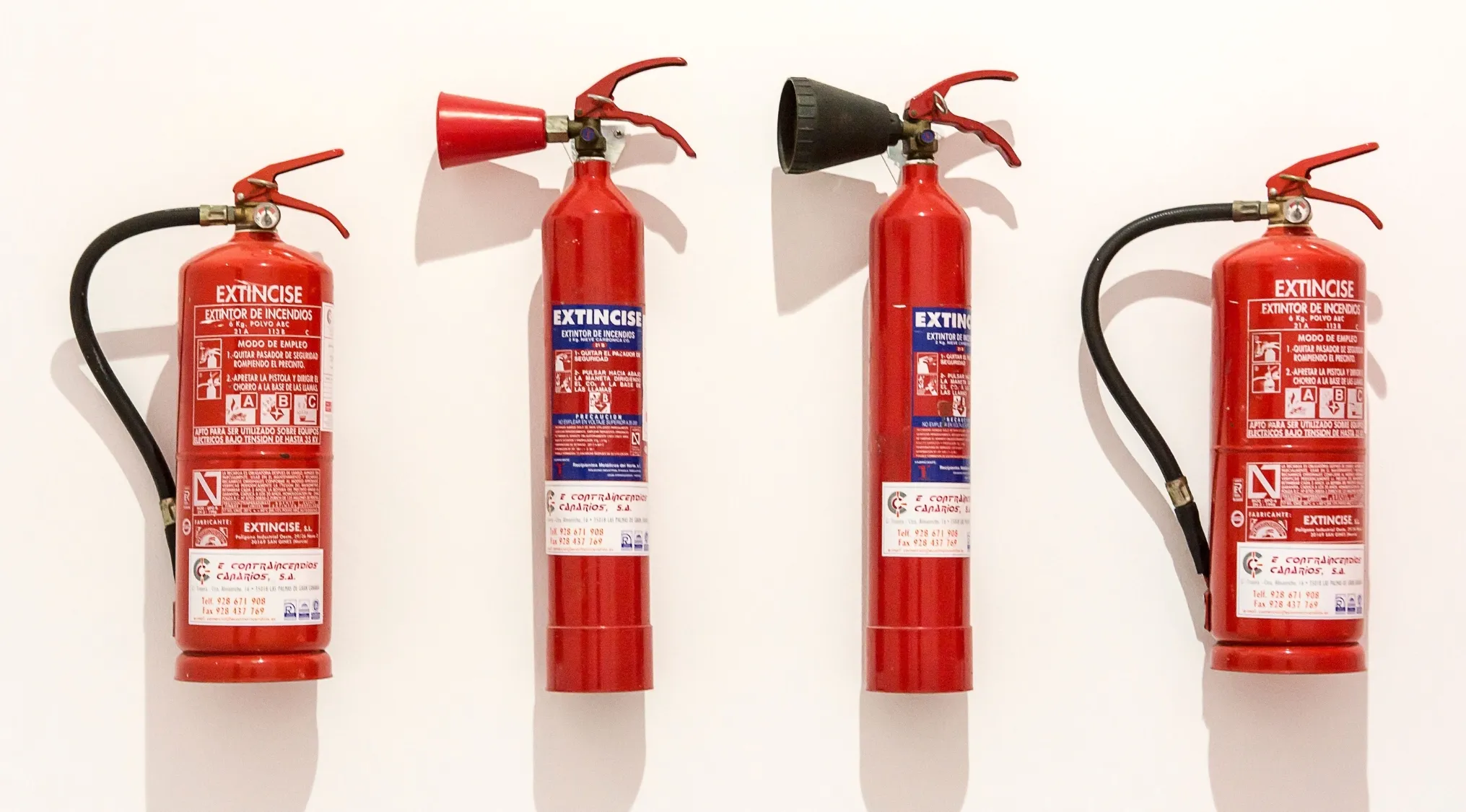 Four red fire extinguishers hung on a white wall, relevant to fire extinguisher replacement schedule discussions.
