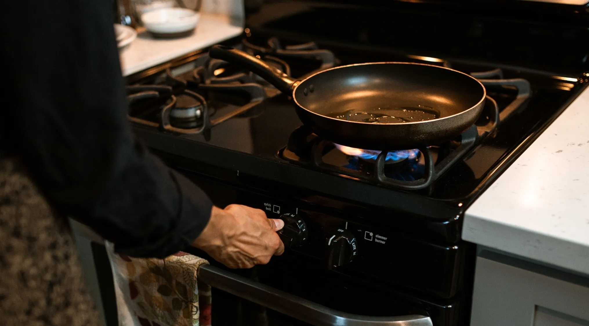 A person adjusts a stove burner with a pan containing oil, illustrating how to preheat a pan for home economics.