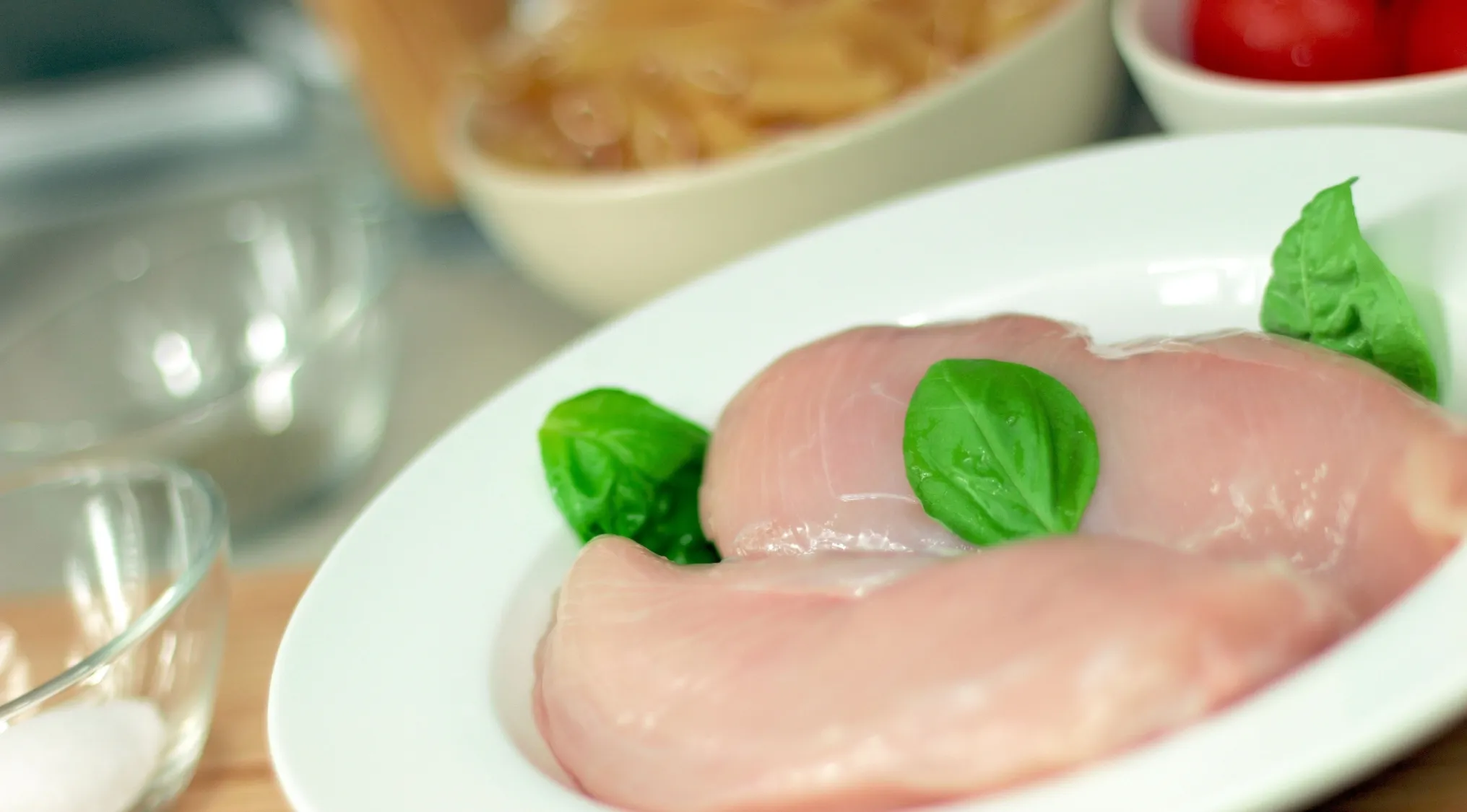 Raw chicken fillets with fresh basil on a white plate, highlighting risks like Salmonella food poisoning.