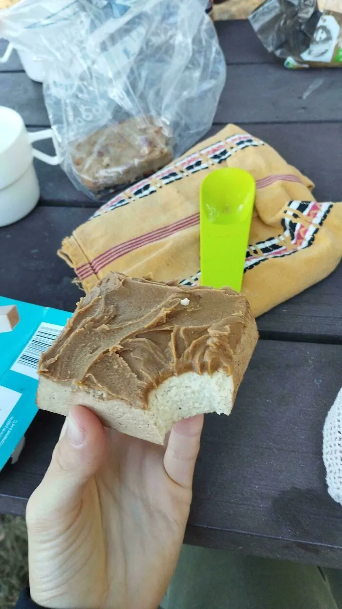 Hand holding a block of butter topped with peanut butter, a questionable food combo.