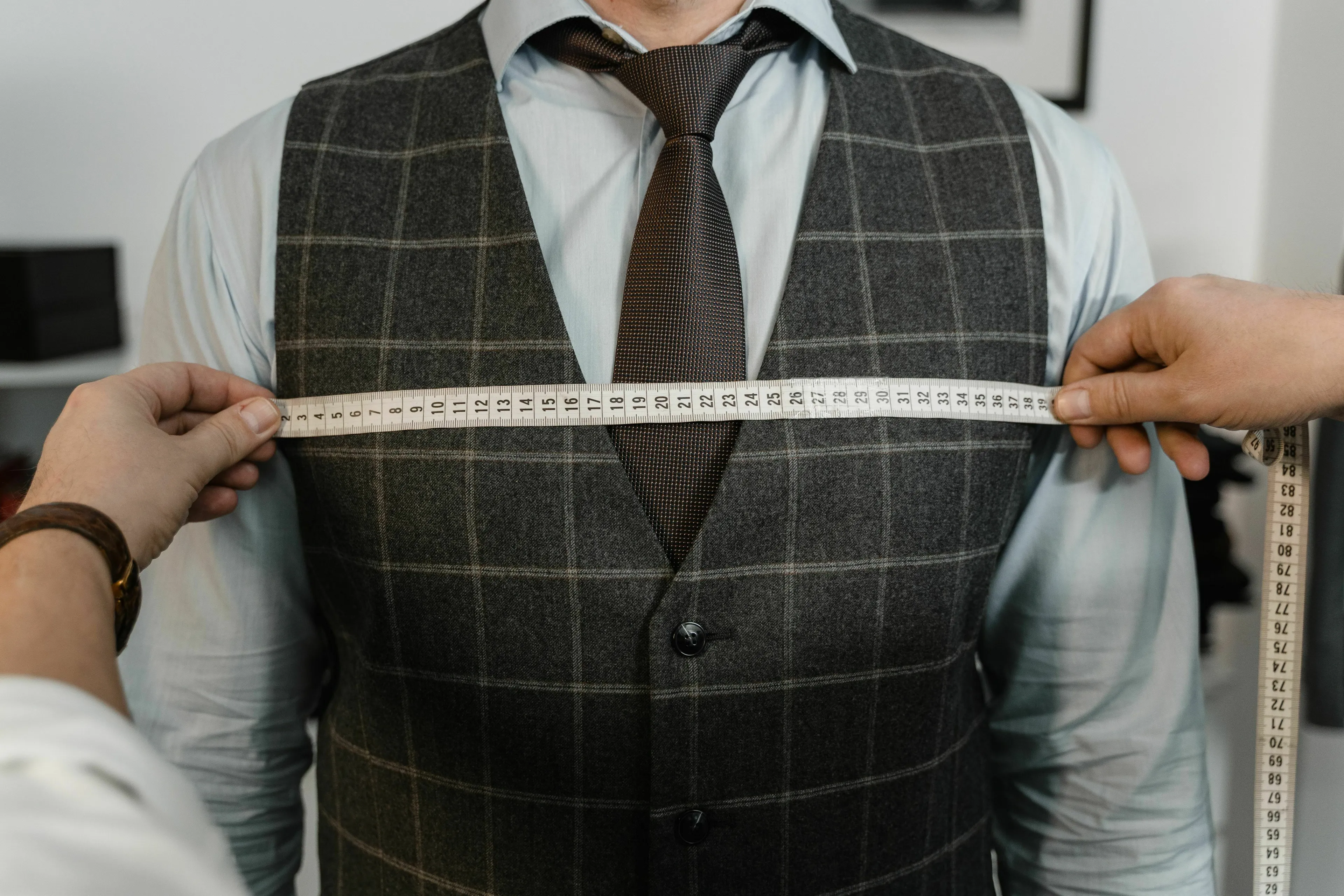 A tailor measuring a man's chest while he wears a plaid vest and tie, perfect for English words quiz.