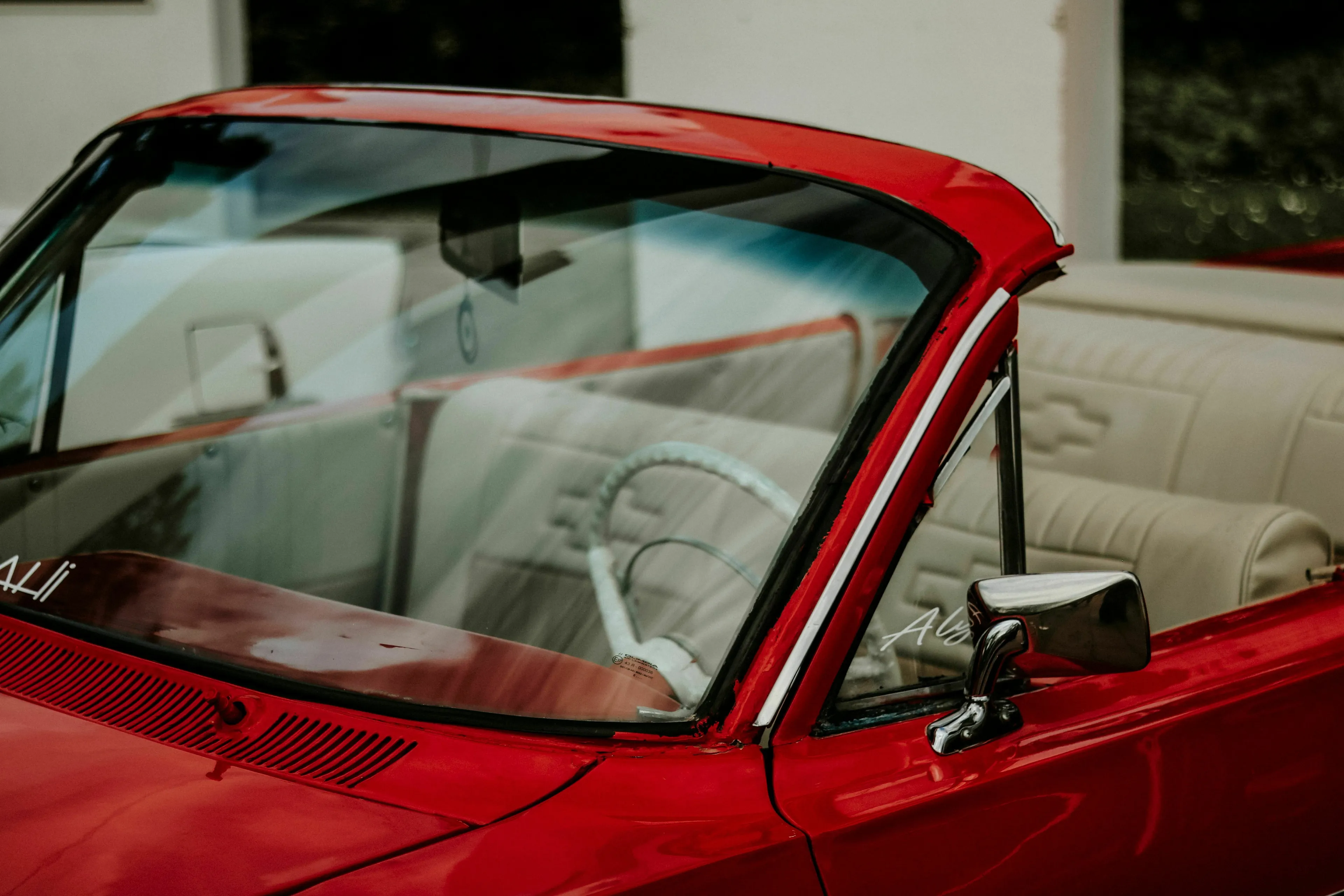 Close-up of the windshield and side mirror of a vintage red car, ideal for an English words quiz about car parts.