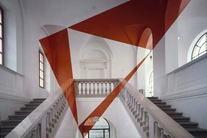 An optical illusion of red geometric shapes overlaid on a grand white staircase, a real photo that makes your brain question if it was edited.