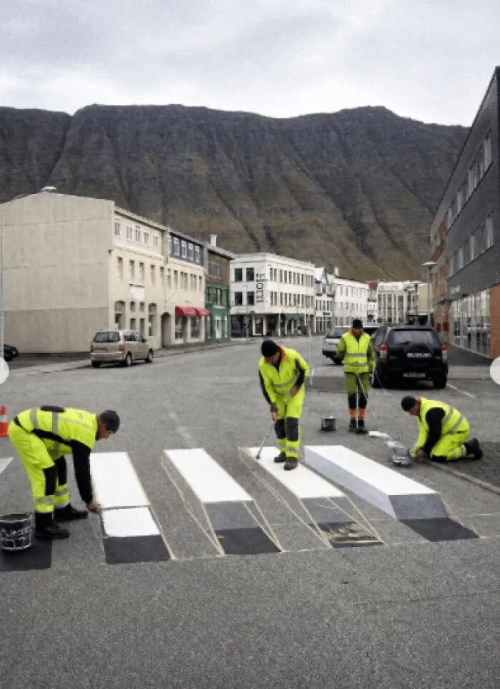 Workers painting a 3D crosswalk on a street, a real photo that makes your brain question if it was edited.