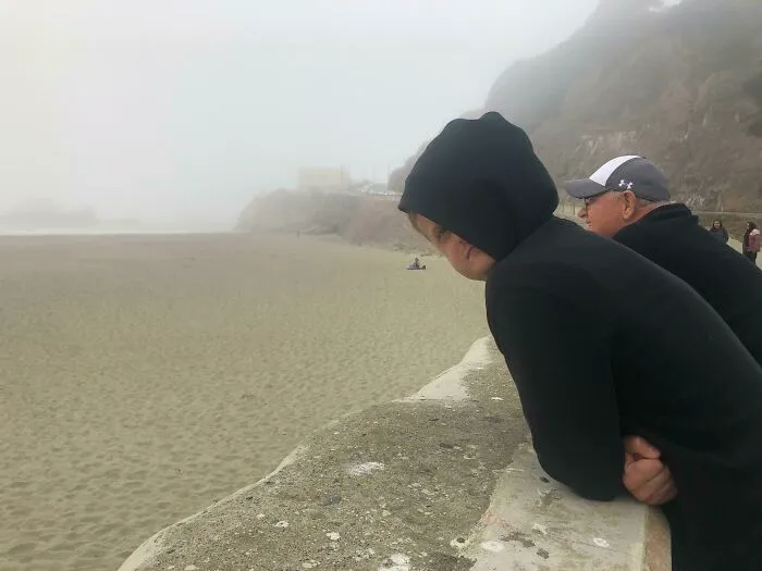 Real photos of people looking out at a foggy beach, making the brain question if they were edited.