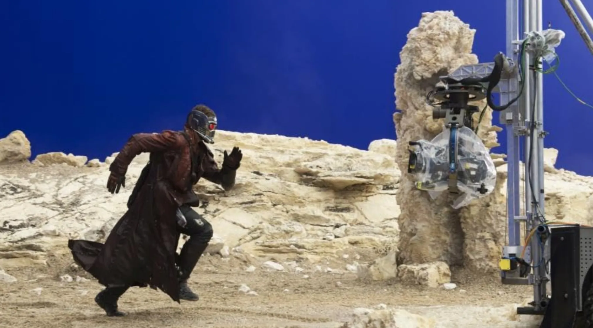 BTS image of a movie set with a character in costume running on a rocky terrain against a blue screen. Guess the movie.