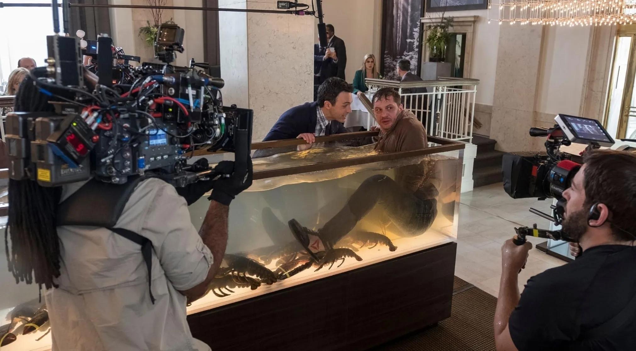 Guess the movie franchise: BTS shot of a man in a lobster tank with another man leaning over it, filming in progress.