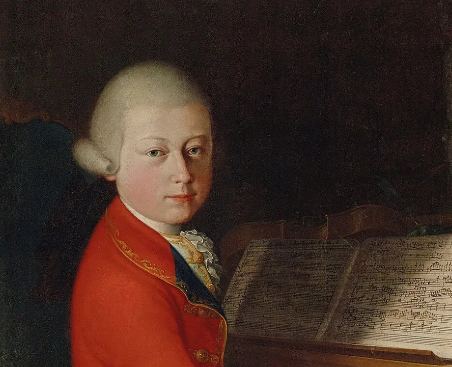 A young Wolfgang Amadeus Mozart in a red jacket, looking at the viewer, with sheet music and a violin beside him.