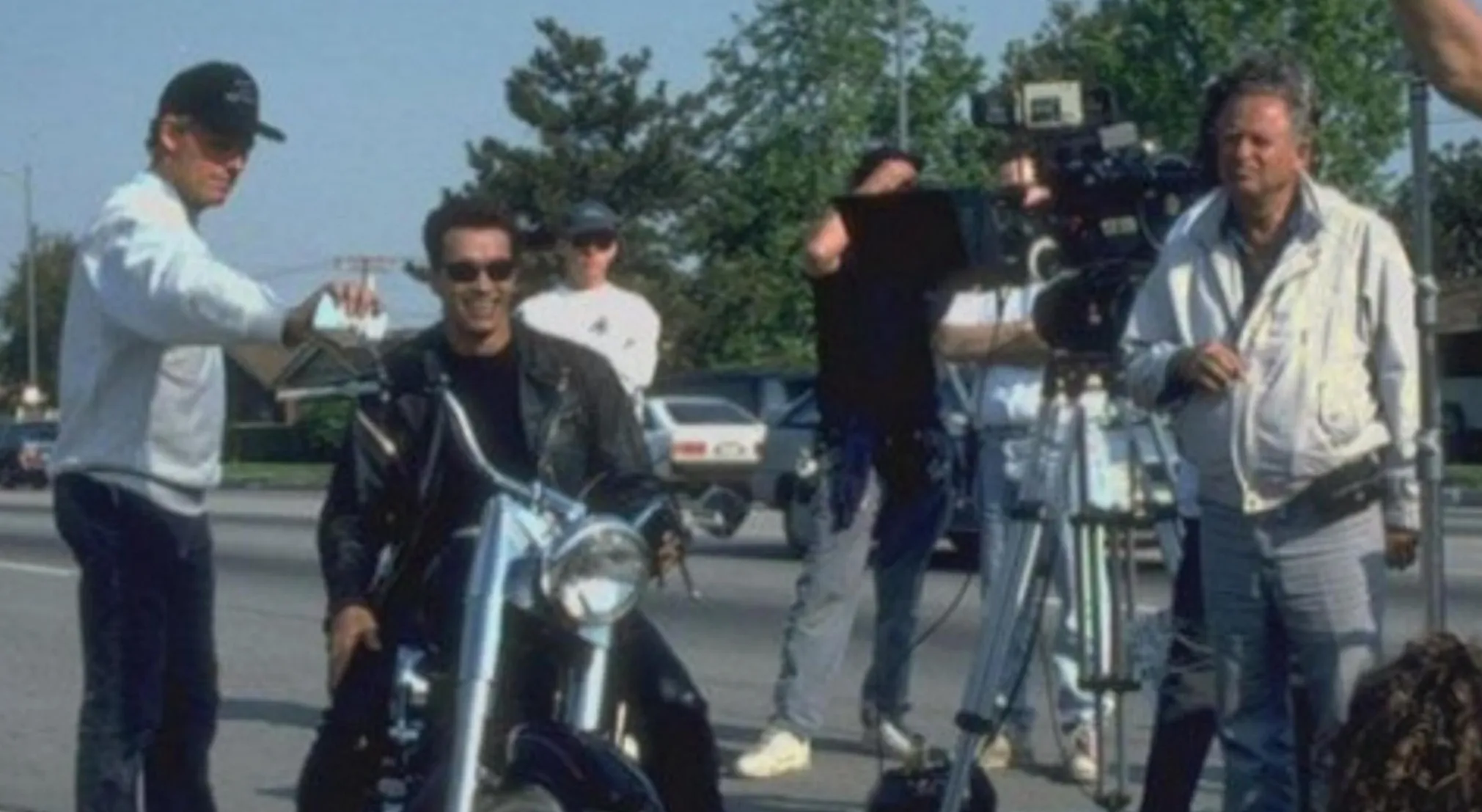 Behind-the-scenes image of Arnold Schwarzenegger on a motorcycle, surrounded by film crew. Guess the movie from this BTS image.