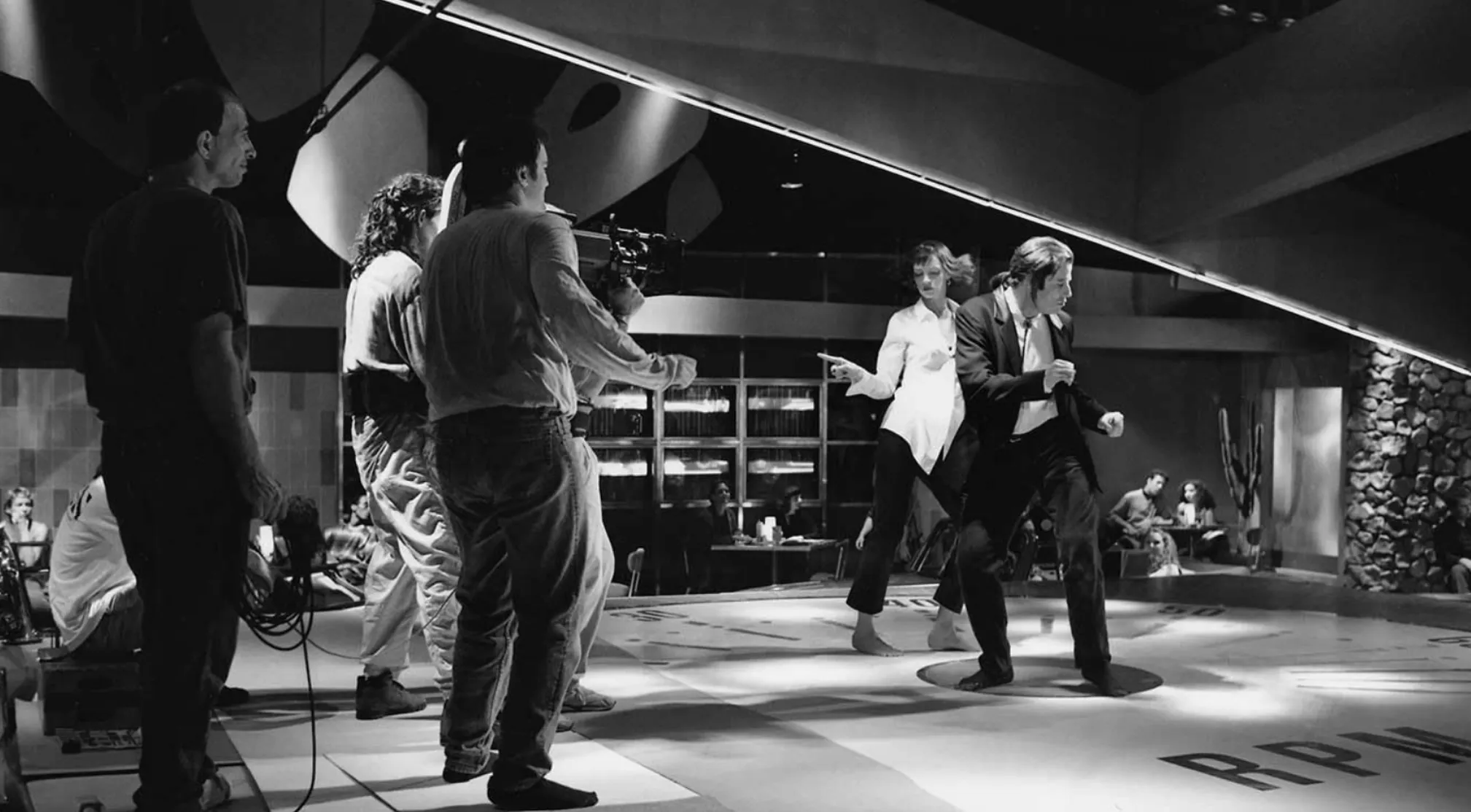 Black and white BTS image of a movie set with a camera crew filming two actors dancing. Guess the movie.