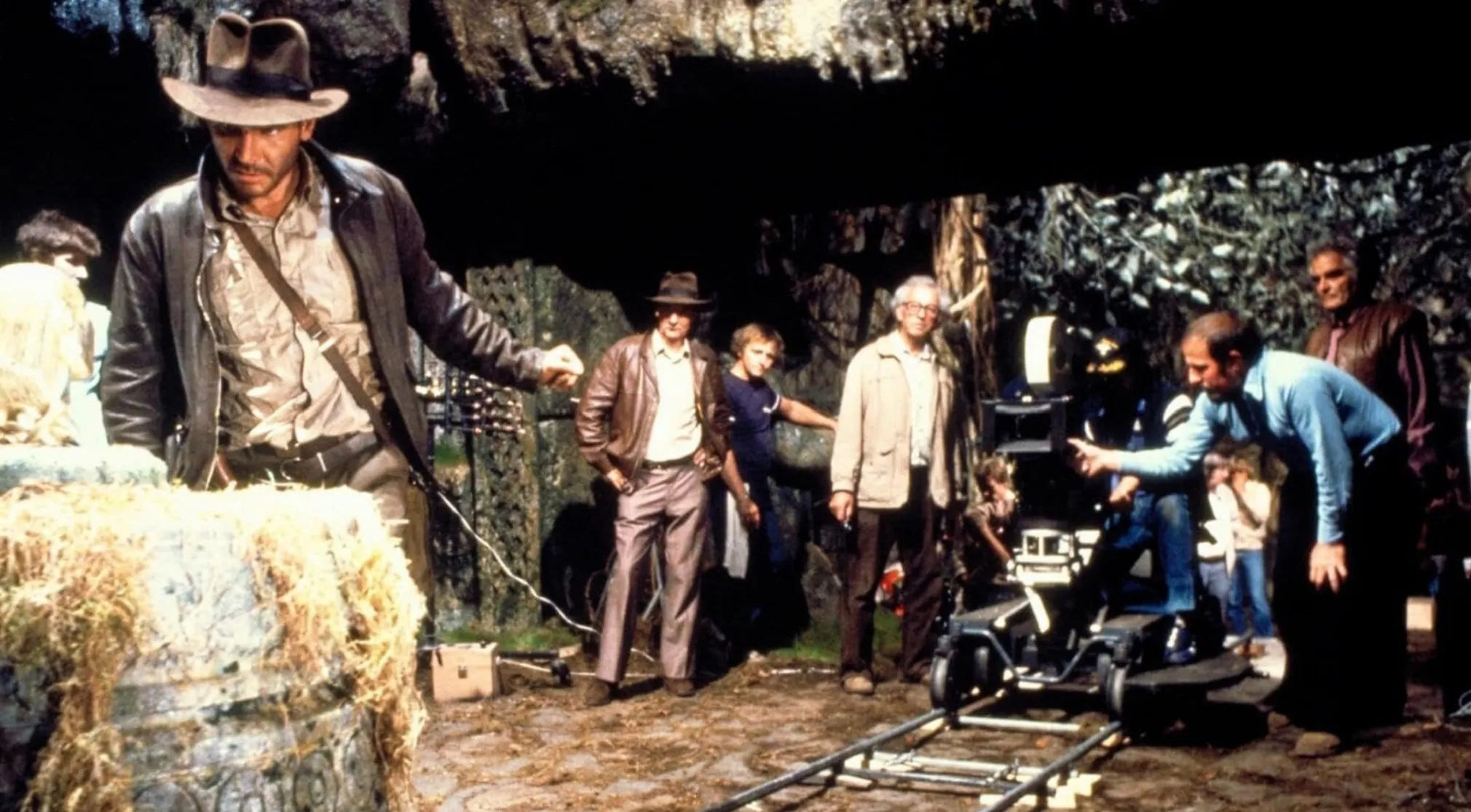 Guess The Movie from a BTS image of Harrison Ford in a fedora, on a movie set with crew and a camera.