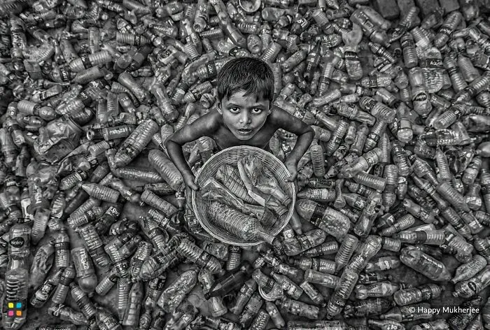 Award-worthy photo from HIPA of a child surrounded by plastic bottles, holding a basket of recycled items.