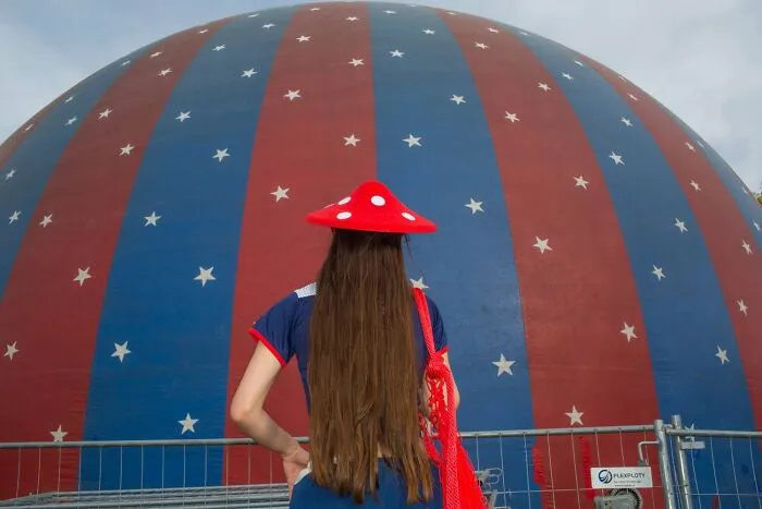 A woman wearing a red mushroom hat looks at a red and blue striped dome with stars, a serendipitous moment captured by a street photographer.
