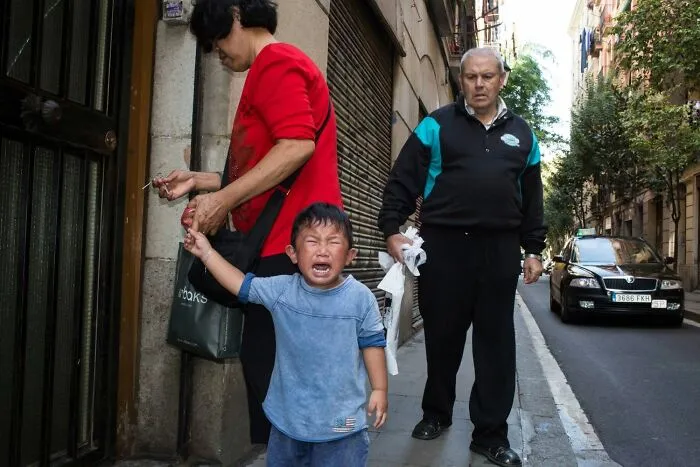 A street photographer captures a serendipitous moment of a crying child with adults on a street in everyday life.