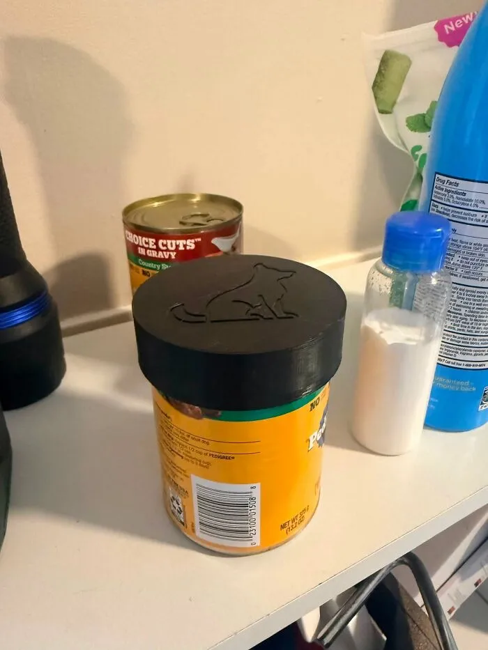 A black 3D-printed lid with a dog silhouette on a container of dog food, a useful thing created with a 3D printer.