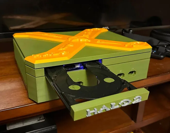 A custom 3D printer case for an Xbox, in green and orange, with the disc tray open revealing Halo 2 text.