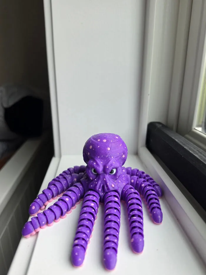 A purple 3D printed octopus with pink suckers on its tentacles and small white dots, sitting on a white surface.