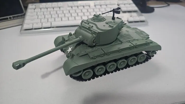A military-green 3D printed tank model on a white surface with a keyboard in the background, a cool thing created with a 3D printer.