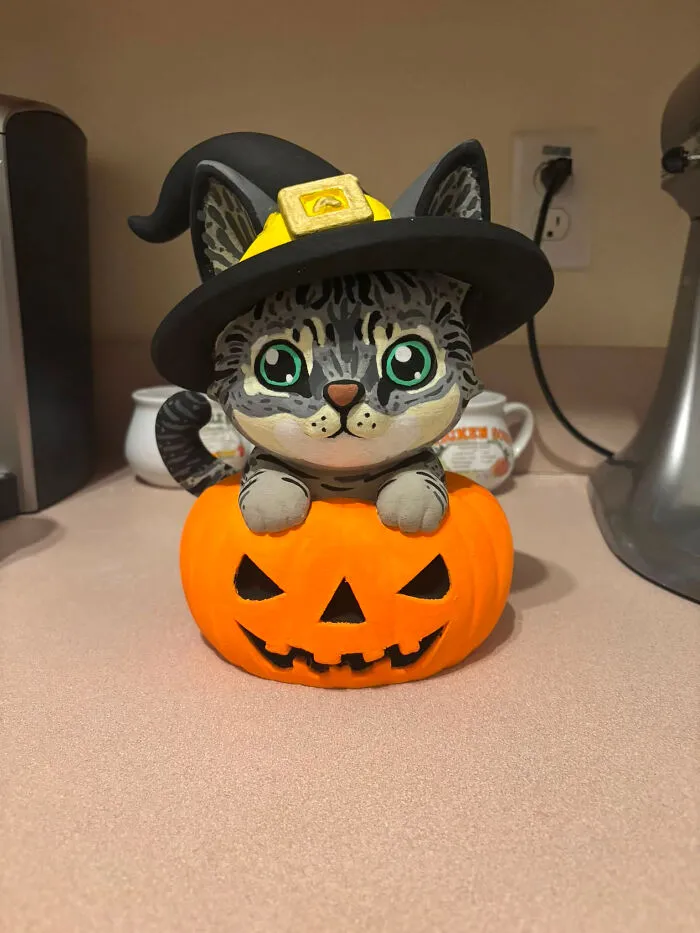 A cute cat figure wearing a witch hat emerging from a pumpkin, a cool 3D printer creation.