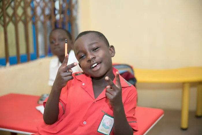 A young Gen Alpha student holding a pencil and making peace signs, depicting Gen Alpha at school.
