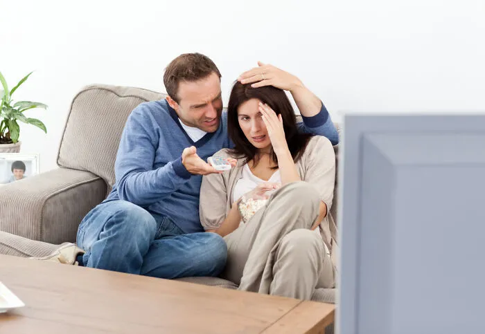 A scared woman watching a video on TV with a man comforting her, for ghosts videos that are hard to explain.