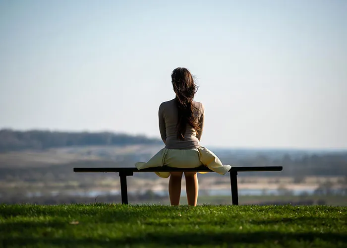 A woman sitting on a bench overlooking a vast landscape, contemplating things we slowly stopped doing.