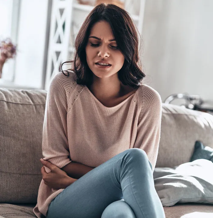 A woman sitting on a couch, holding her stomach in discomfort. A hard truth for women.
