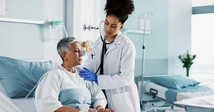A compassionate doctor from the medical industry checks on an elderly patient in a hospital bed with a stethoscope.