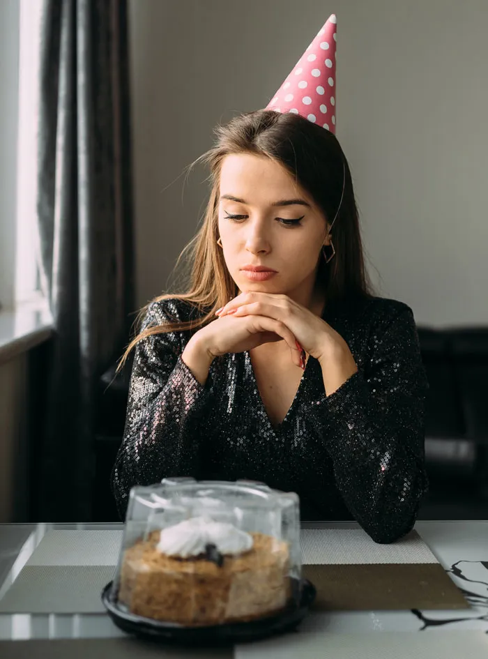 A sad woman in a party hat looking at a cake, contemplating hard truths that women learned.
