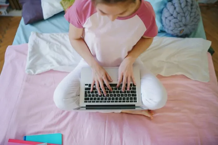 A person typing on a laptop while sitting on a bed, under my roof rules backfired on parents.