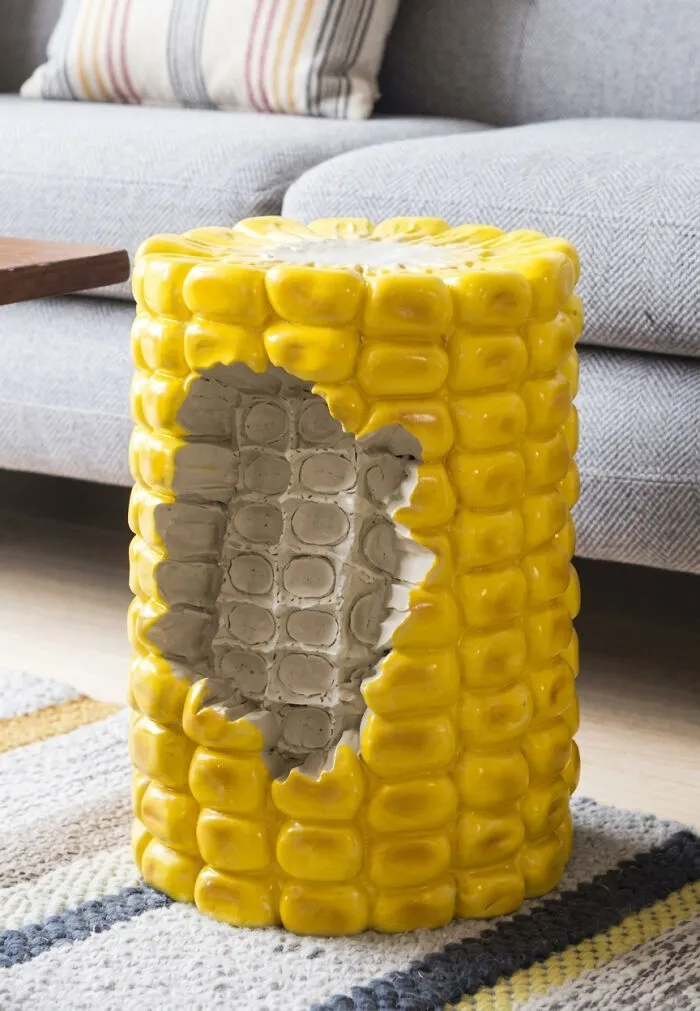 A bizarre furniture design of a stool shaped like a half-eaten corn cob, showing yellow kernels and a white core.