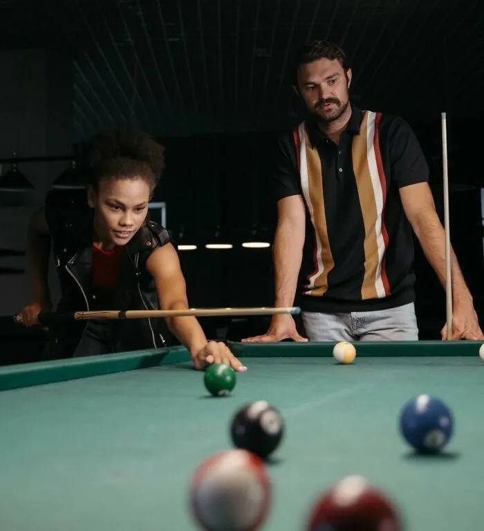 A woman plays pool on a first date while a man watches, potentially revealing first date red flags.
