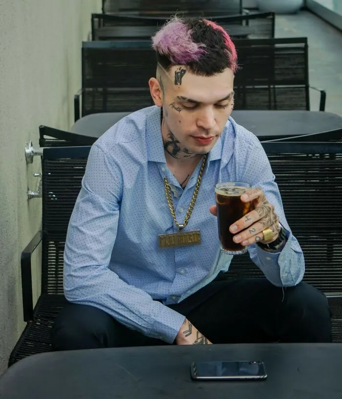 Man with tattoos and pink hair holding a drink, a potential first date red flag if judgment is involved.