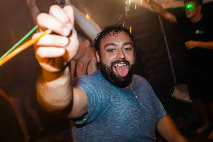 A man at a party with his tongue out and holding glow sticks, portraying men giving partners an ick.