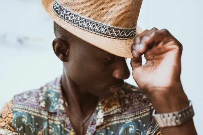A man adjusting a stylish straw hat, looking downwards, potentially giving his partners an ick.