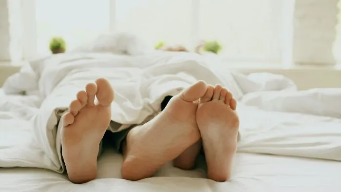 Two pairs of feet under a duvet in bed, representing partners giving each other the ick they can't get over.