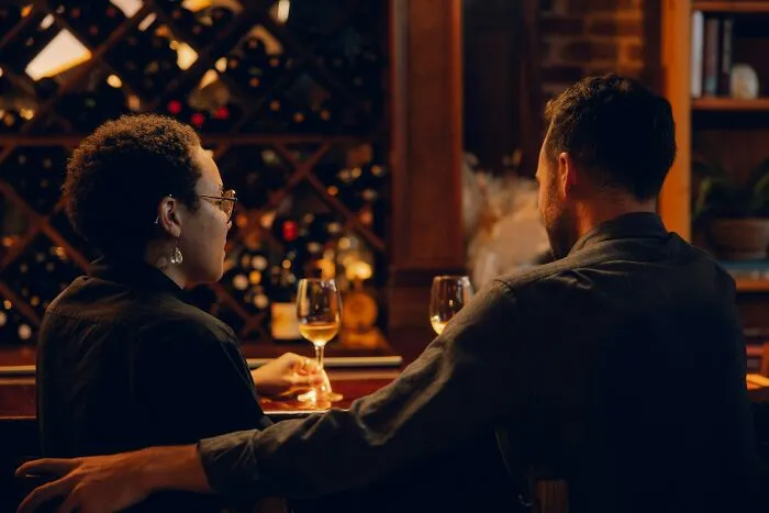 A couple sitting at a bar with wine, illustrating partners giving each other the ick they can't get over.
