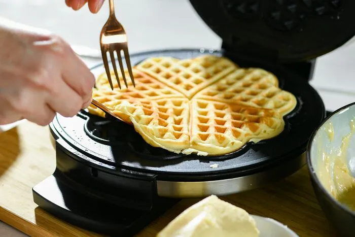 A person removing a heart-shaped waffle from a waffle maker, illustrating a daily activity that might cause an ick.