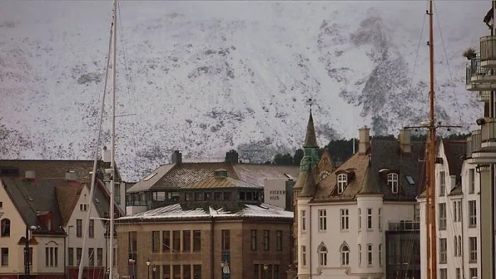 Historic buildings with pointed roofs in front of snow-covered mountains, a real photo that makes your brain question if it was edited.