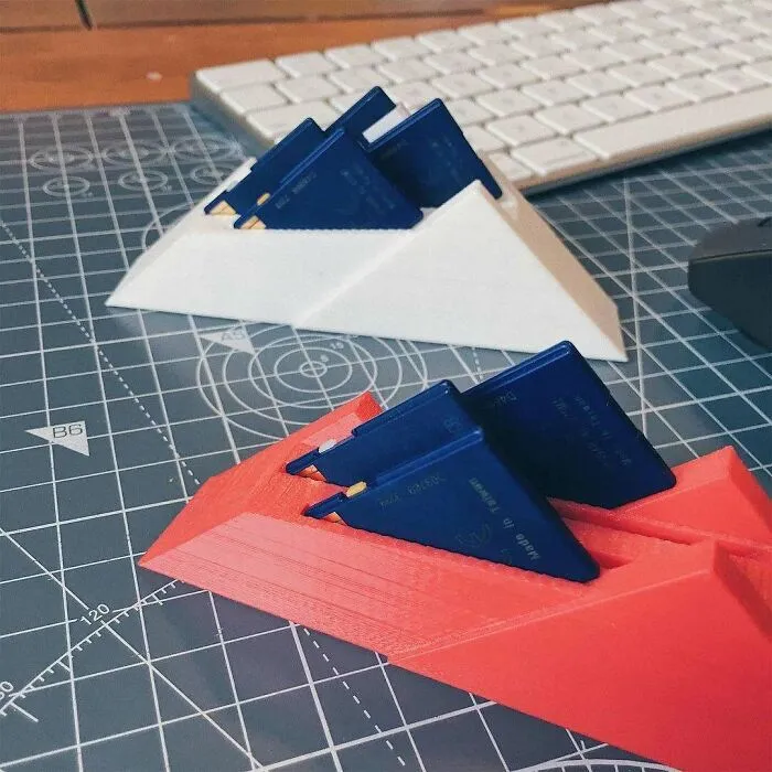 A close-up of two 3D printing creations, one white and one red, holding small blue items on a grey cutting mat. Amazing 3D printing creations.