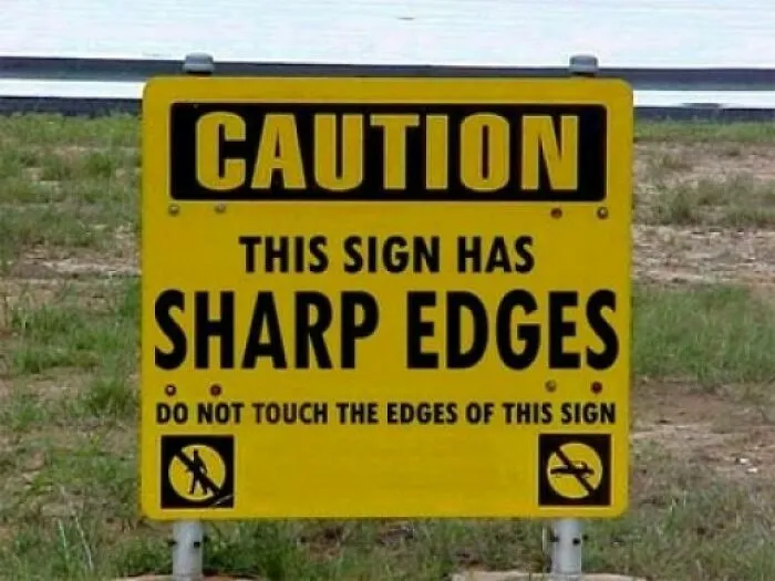 Hilariously dumb warning label: A bright yellow sign reads, CAUTION THIS SIGN HAS SHARP EDGES. Do not touch.