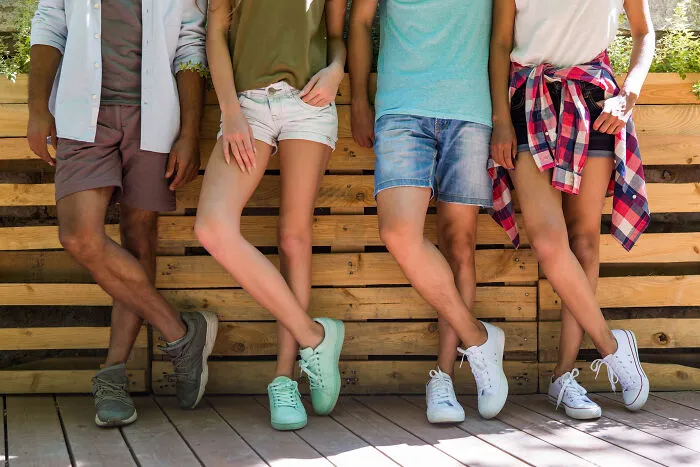 Four young people standing together, their crossed legs showing various styles of casual shorts and sneakers, illustrating house etiquette.