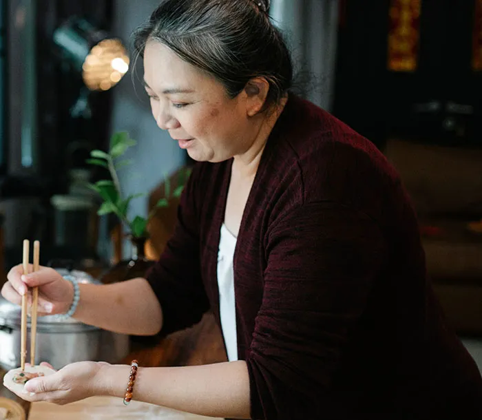An Asian woman preparing food with chopsticks, showcasing a moment of cultural sharing in intercultural relationships.