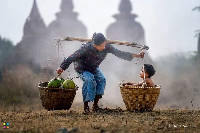 An old woman carrying a child and coconuts in baskets, captured in award-worthy photos from HIPA.