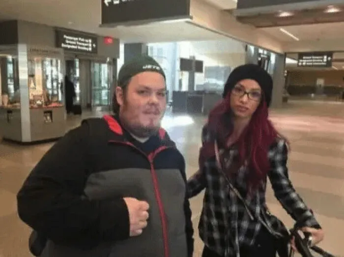 A celebrity, Sasha Banks, looks uncomfortable as a fan stands close for a photo in an airport.