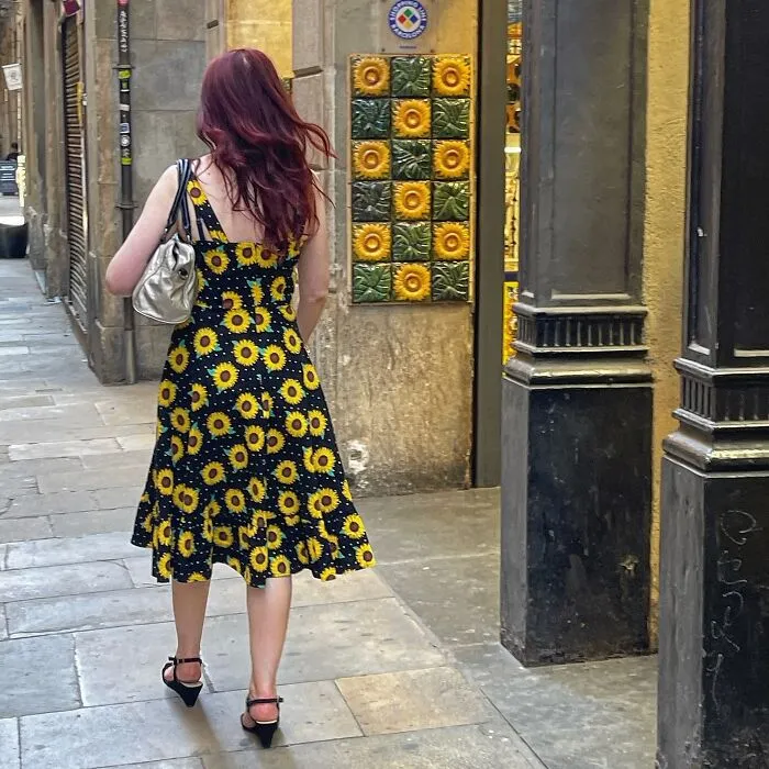 Divertida foto accidental de una mujer con un vestido de girasoles caminando por una calle adoquinada.